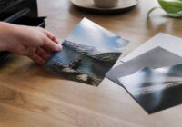 Close-up van een persoon die een verse foto-afdruk op een houten tafel legt naast mat en glanzend fotopapier