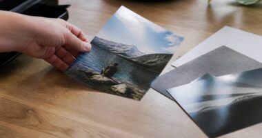 Close-up van een persoon die een verse foto-afdruk op een houten tafel legt naast mat en glanzend fotopapier